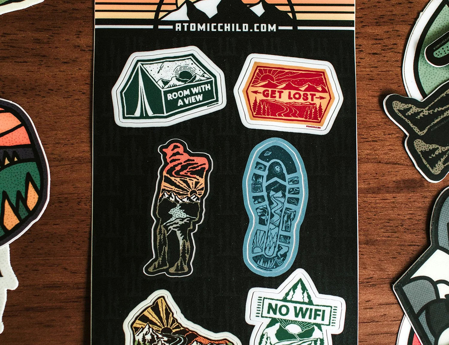 Atomicchild Hiking Mini Sticker Sheet with tent, hiking boot, No WiFi and Get Lost stickers on a wooden table