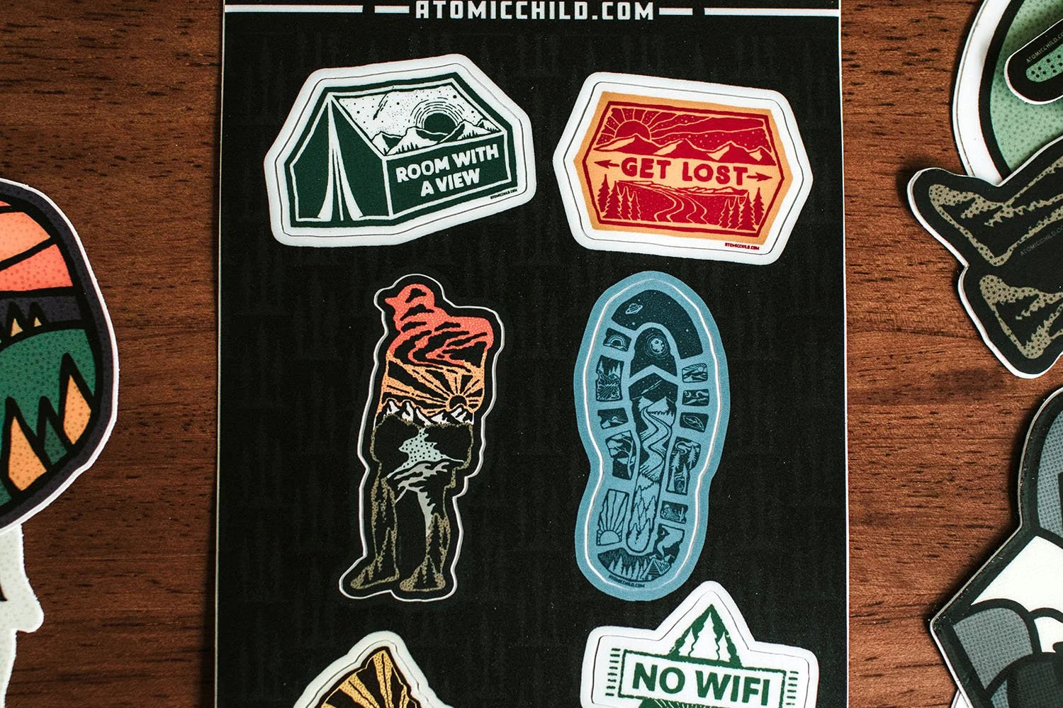 Atomicchild Hiking Mini Sticker Sheet with tent, hiking boot, No WiFi and Get Lost stickers on a wooden table
