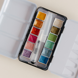 Bailey Rae Studio 12 Color Travel Metallic Watercolor Paint Palette, open tin showing twelve shimmering metallic watercolor pans and a brush