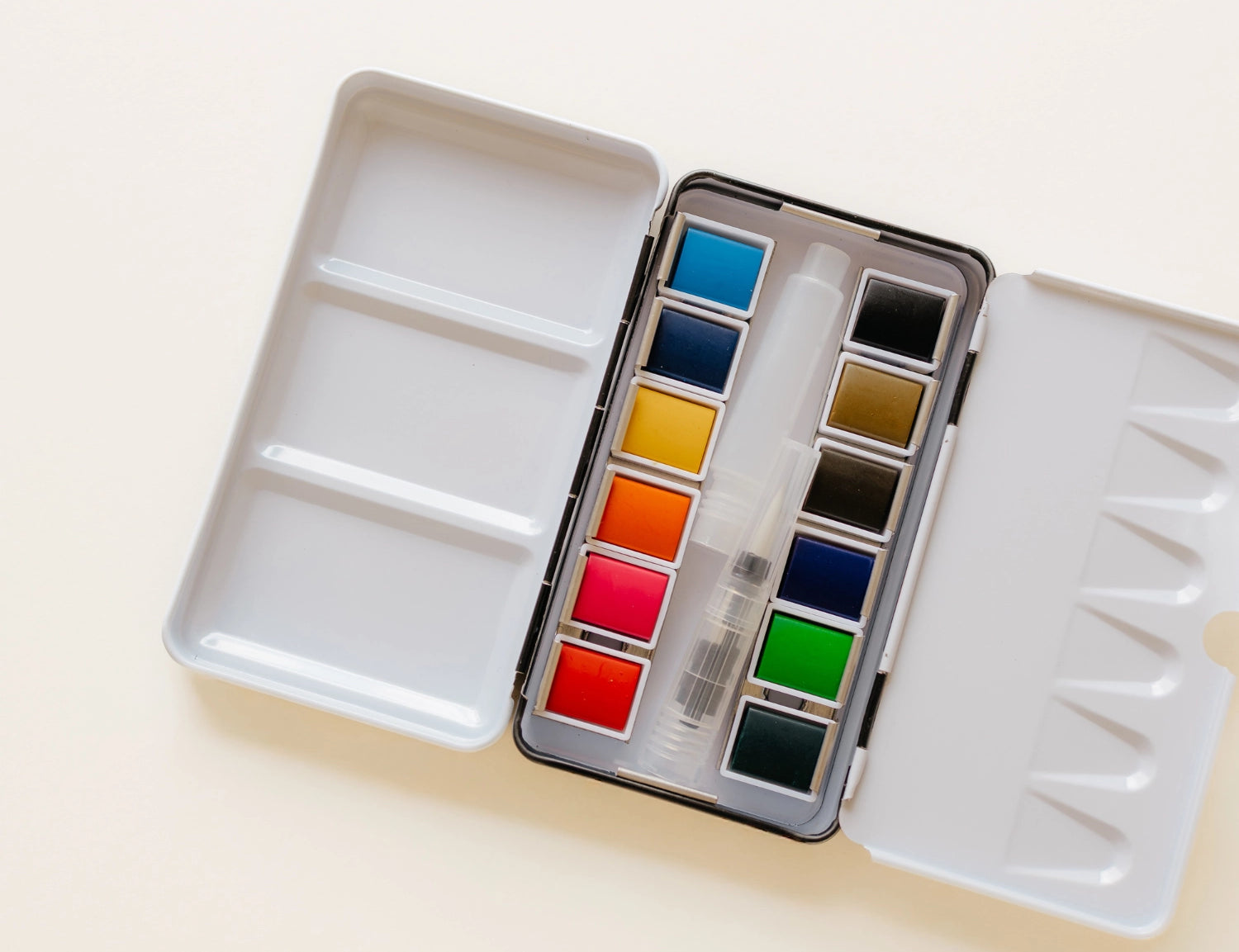 Bailey Rae Studio 12 Color Mini-Travel Paint Palette, open silver tin with twelve watercolor pans in blues, greens, reds, and yellows on a cream background