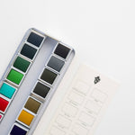 Bailey Rae Studio 24 Color Watercolor Paint Palette, close-up of green, teal, brown and grey pans beside the swatch chart card