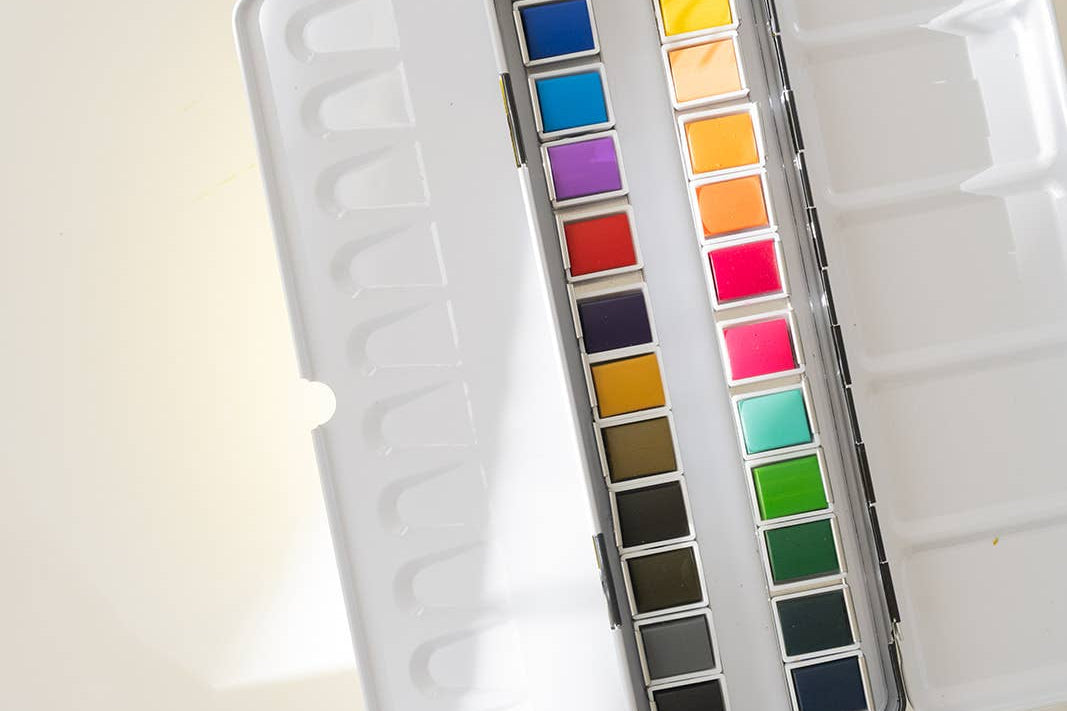 Bailey Rae Studio 24 Color Watercolor Paint Palette, open tin with mixing wells and twenty-four colorful pans in soft light on white