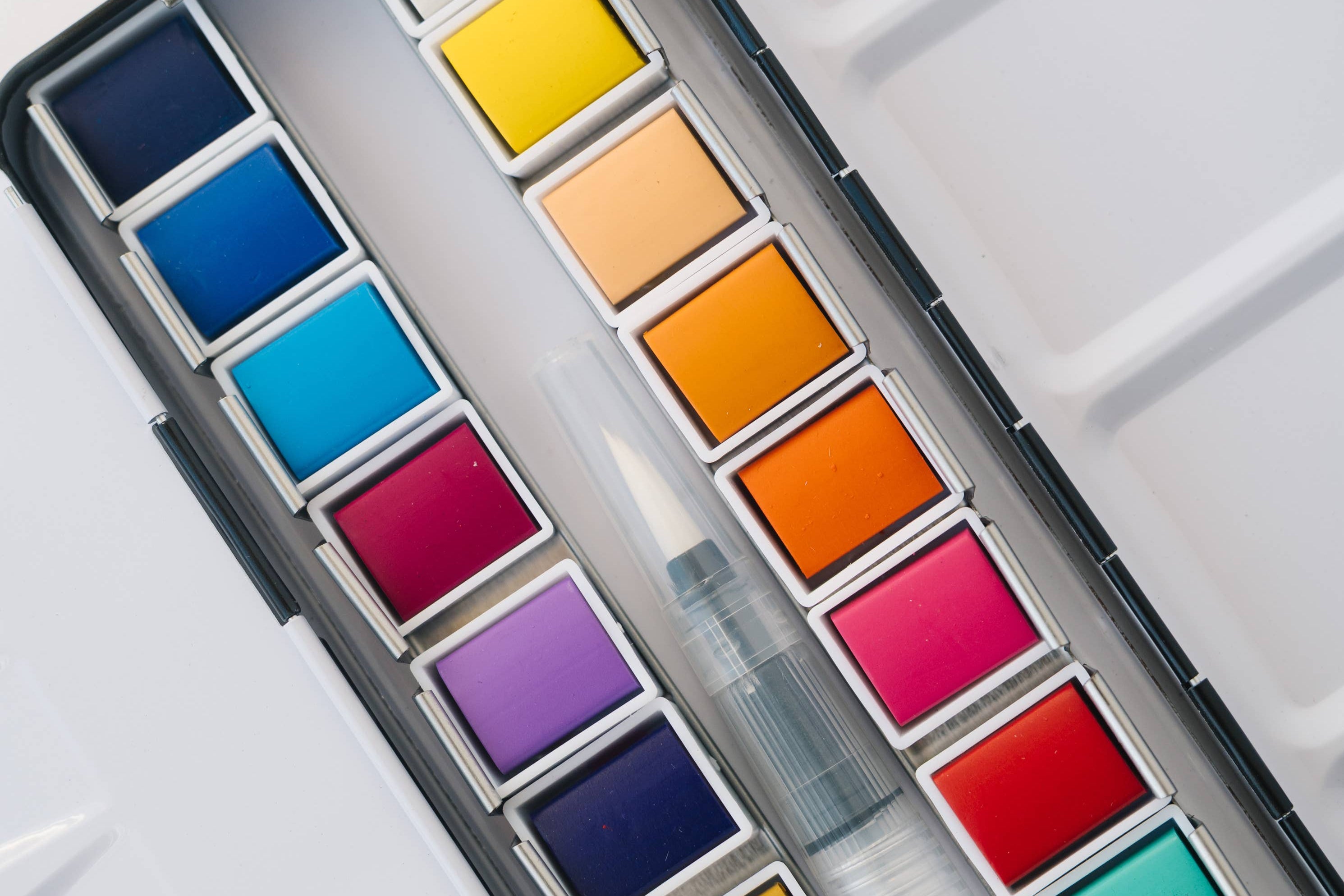 Bailey Rae Studio 24 Color Watercolor Paint Palette, close-up of bright yellow, orange, red, pink and blue watercolor pans with the water brush
