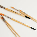 Bailey Rae Studio Filbert Watercolor Brushes with wooden handles scattered on a white surface