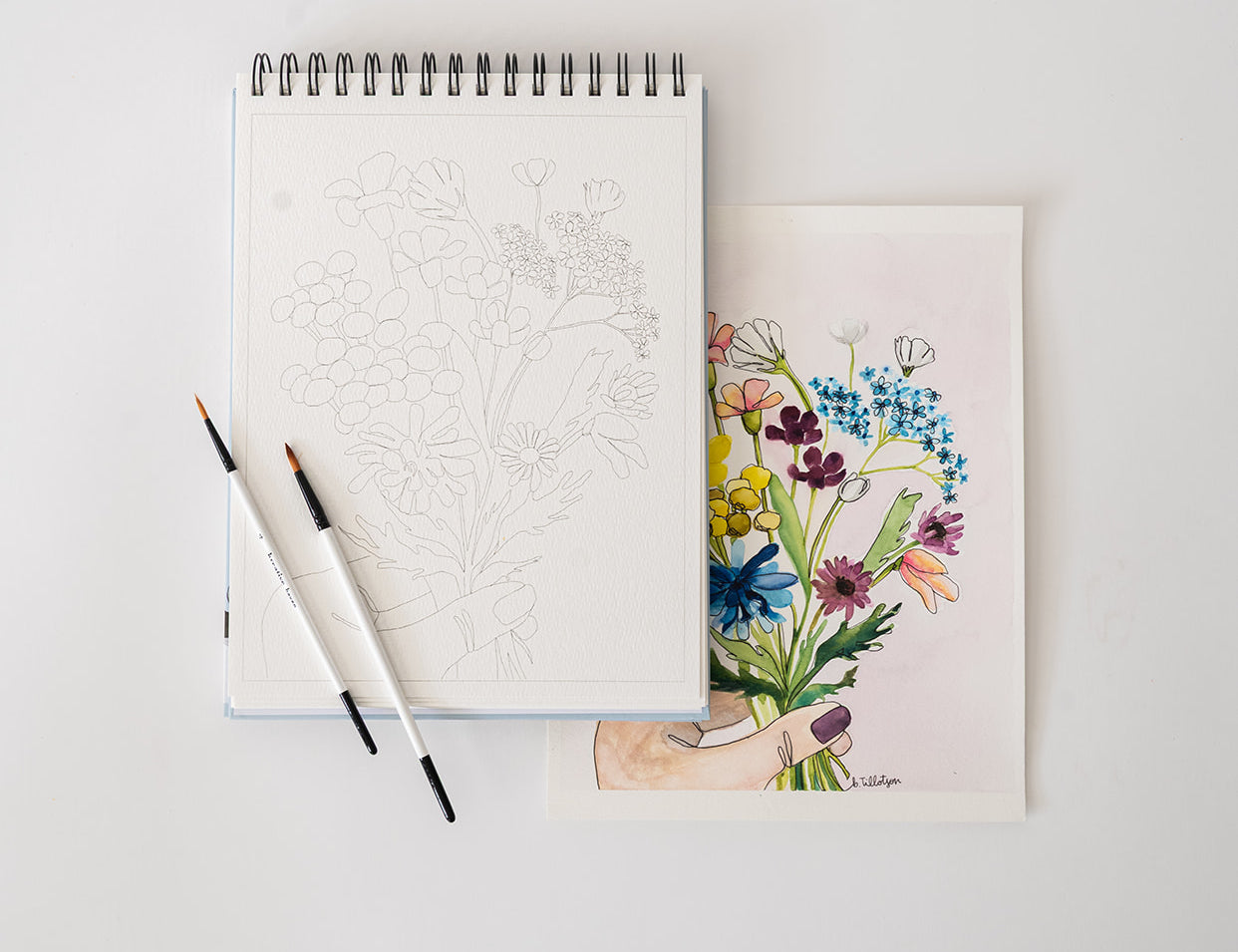 Bailey Rae Studio Floral Watercoloring Book open to an outline page with brushes and a finished floral painting