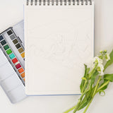 Bailey Rae Studio Landscape Watercoloring Book open to a mountain outline with a paint palette and flowers