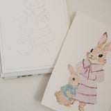 Bailey Rae Studio Mini A Little Bit of Spring Watercoloring Book, outline page beside a finished watercolor of a bunny in a pink dress