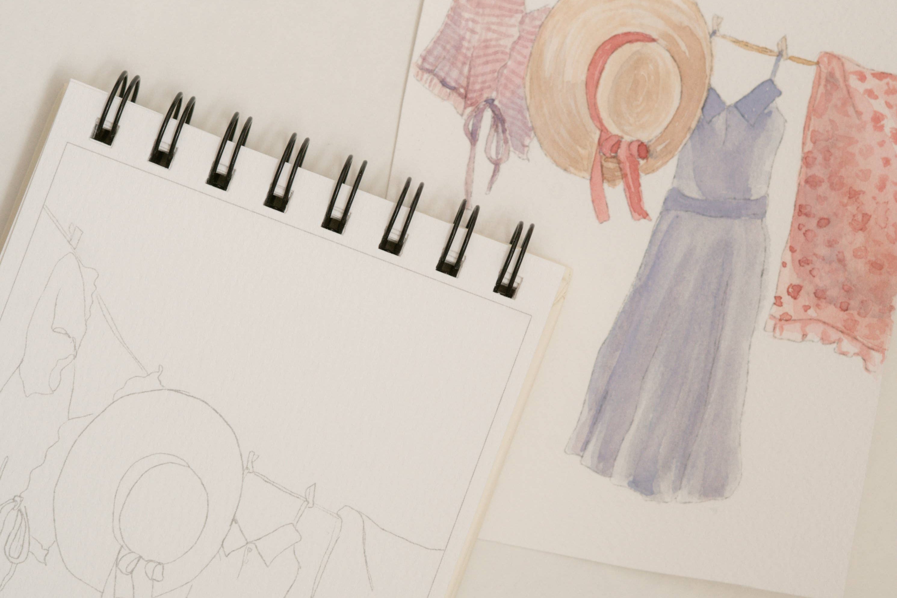 Bailey Rae Studio Mini A Little Bit of Spring Watercoloring Book, clothesline outline page beside a painted line of dresses and a straw hat