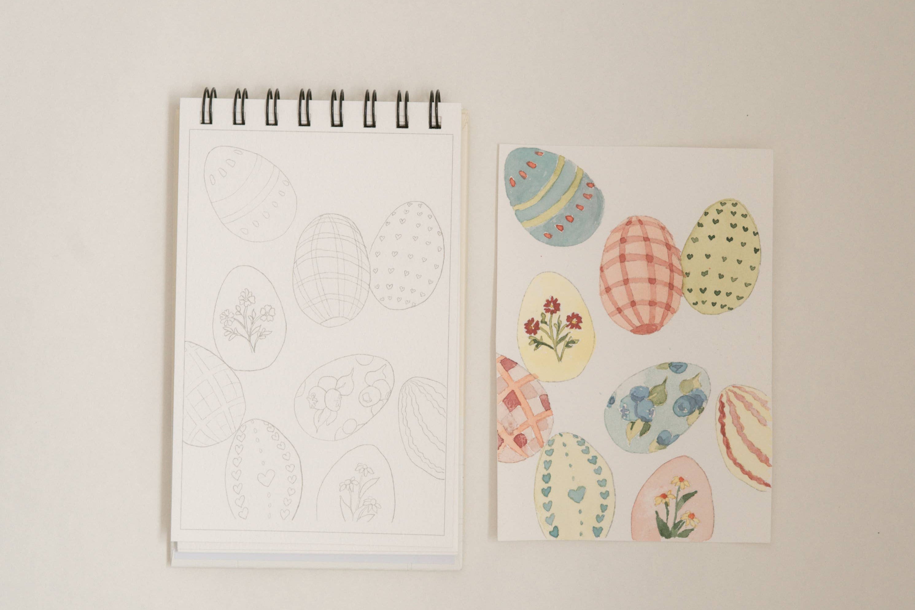 Bailey Rae Studio Mini A Little Bit of Spring Watercoloring Book, Easter egg outline page beside painted pastel patterned eggs