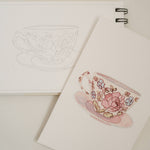 Bailey Rae Studio Mini A Little Bit of Spring Watercoloring Book, teacup outline page beside a painted pink floral teacup