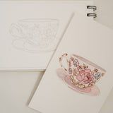 Bailey Rae Studio Mini A Little Bit of Spring Watercoloring Book, teacup outline page beside a painted pink floral teacup