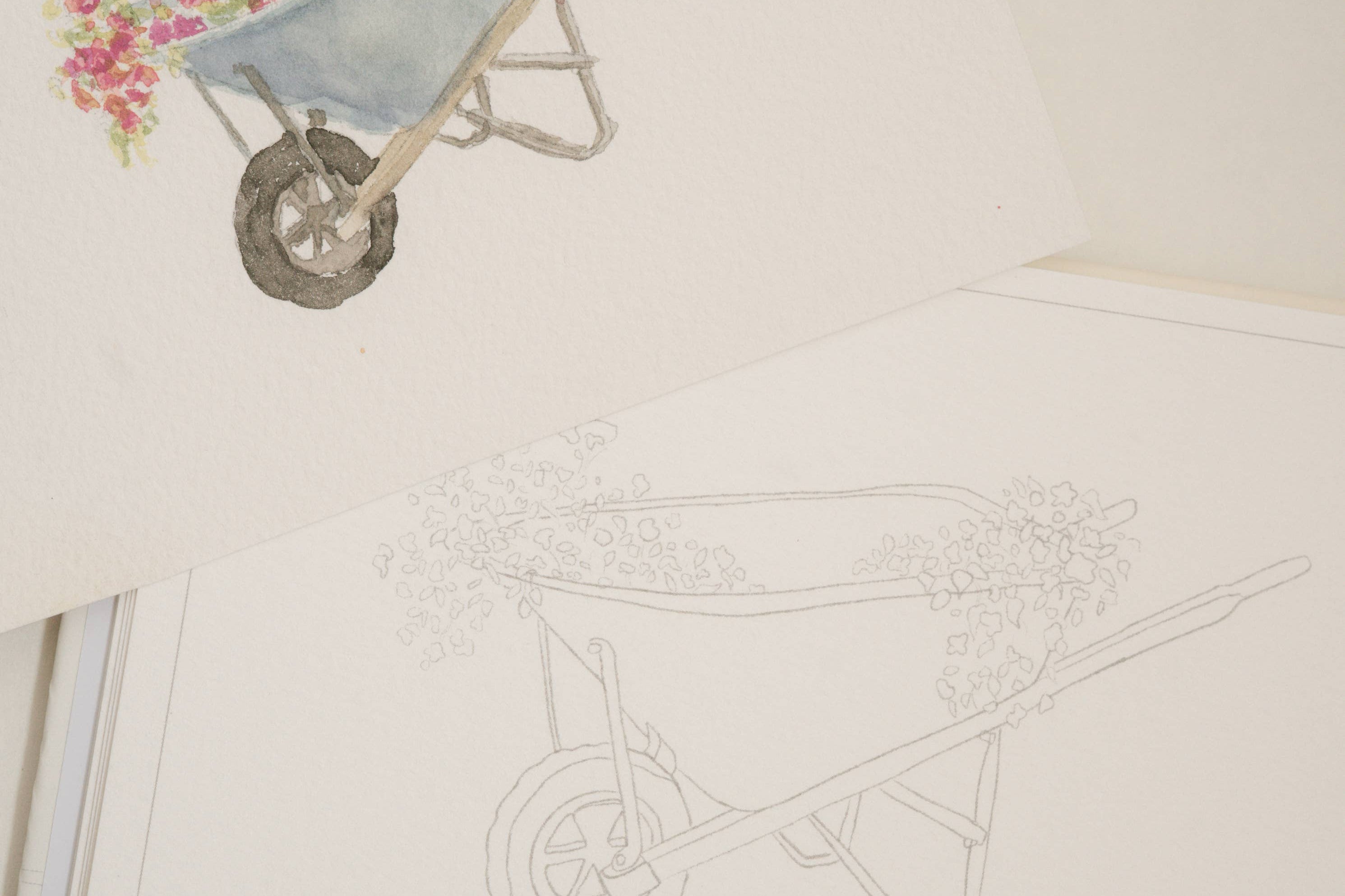 Bailey Rae Studio Mini A Little Bit of Spring Watercoloring Book, wheelbarrow outline page beside a painted wheelbarrow of pink flowers