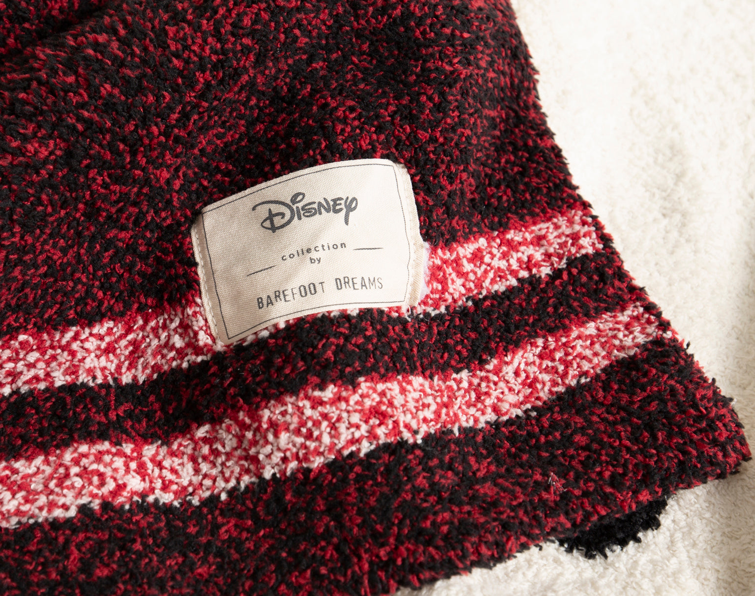 Close-up of the Disney and Barefoot Dreams label on the burgundy striped side of the Classic Disney Baby Blanket