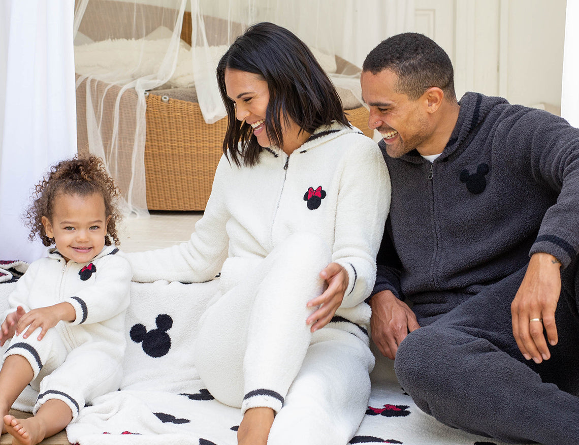 Family in matching pajamas sitting on the Barefoot Dreams Classic Disney Throw in a bright living room
