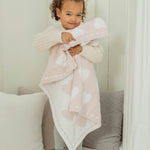 Toddler hugging the Barefoot Dreams CozyChic Dream Receiving Blanket in Hearts, pink with white hearts