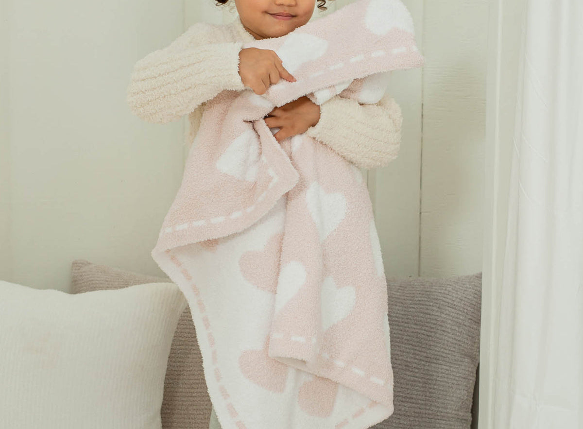 Toddler hugging the Barefoot Dreams CozyChic Dream Receiving Blanket in Hearts, pink with white hearts
