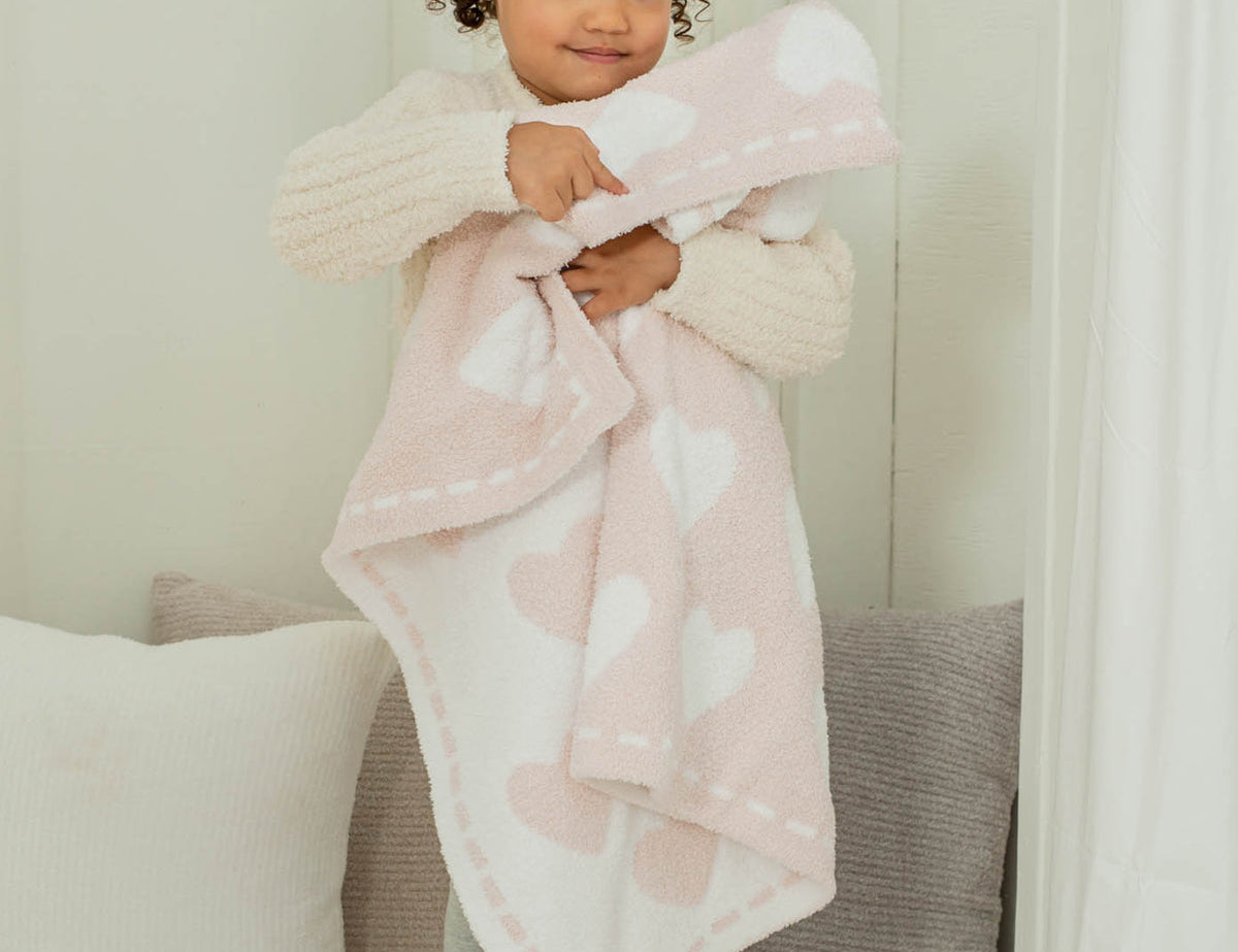 Toddler hugging the Barefoot Dreams CozyChic Dream Receiving Blanket in Hearts, pink with white hearts