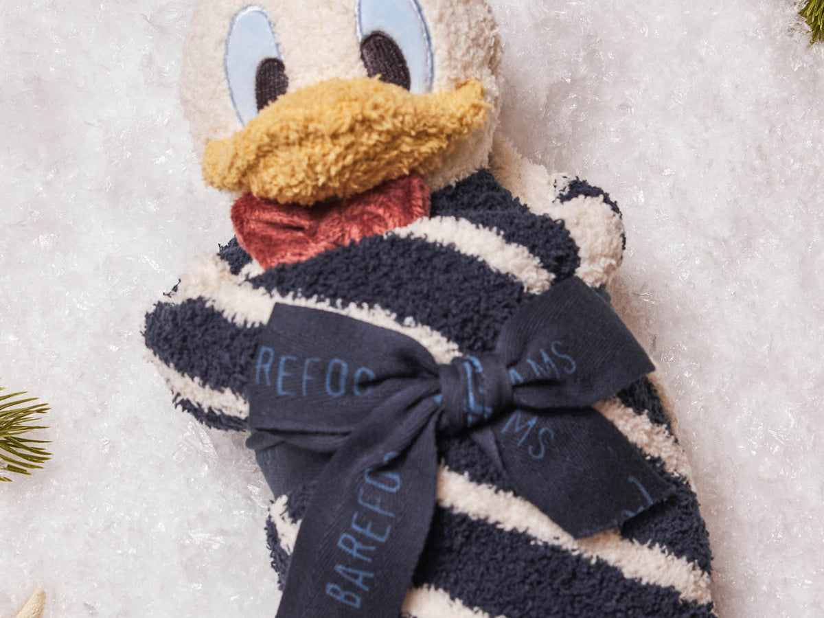 Barefoot Dreams Disney Blanket Buddie in Donald Duck rolled and tied with a ribbon on a snowy background