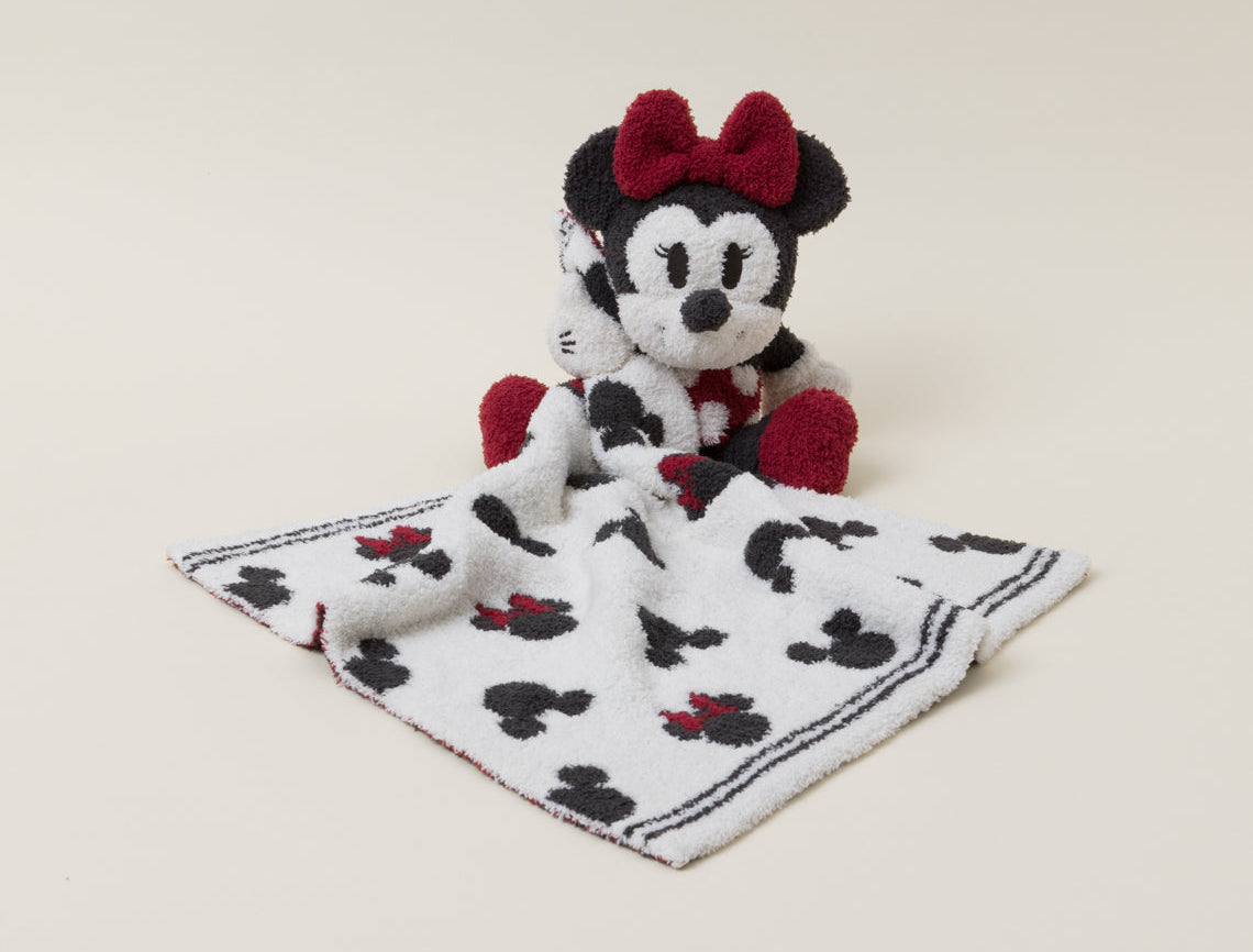 Barefoot Dreams Disney Blanket Buddie in Minnie Mouse laid flat on a Mickey-print blanket