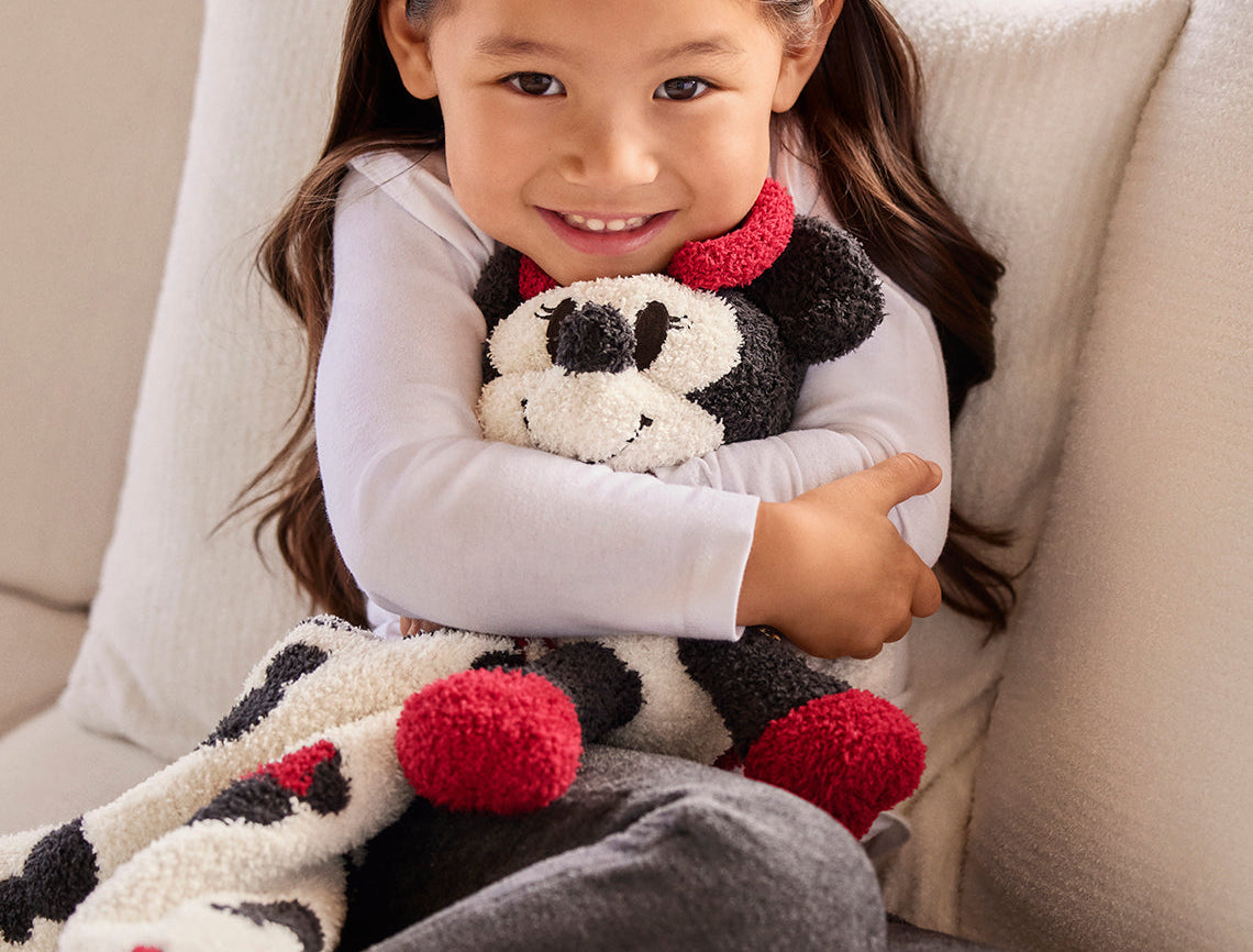 Smiling girl hugging a Barefoot Dreams Disney Blanket Buddie in Minnie Mouse