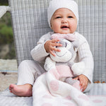 Smiling baby in a white hat holding a Barefoot Dreams Disney Blanket Buddie in Pink Bunny