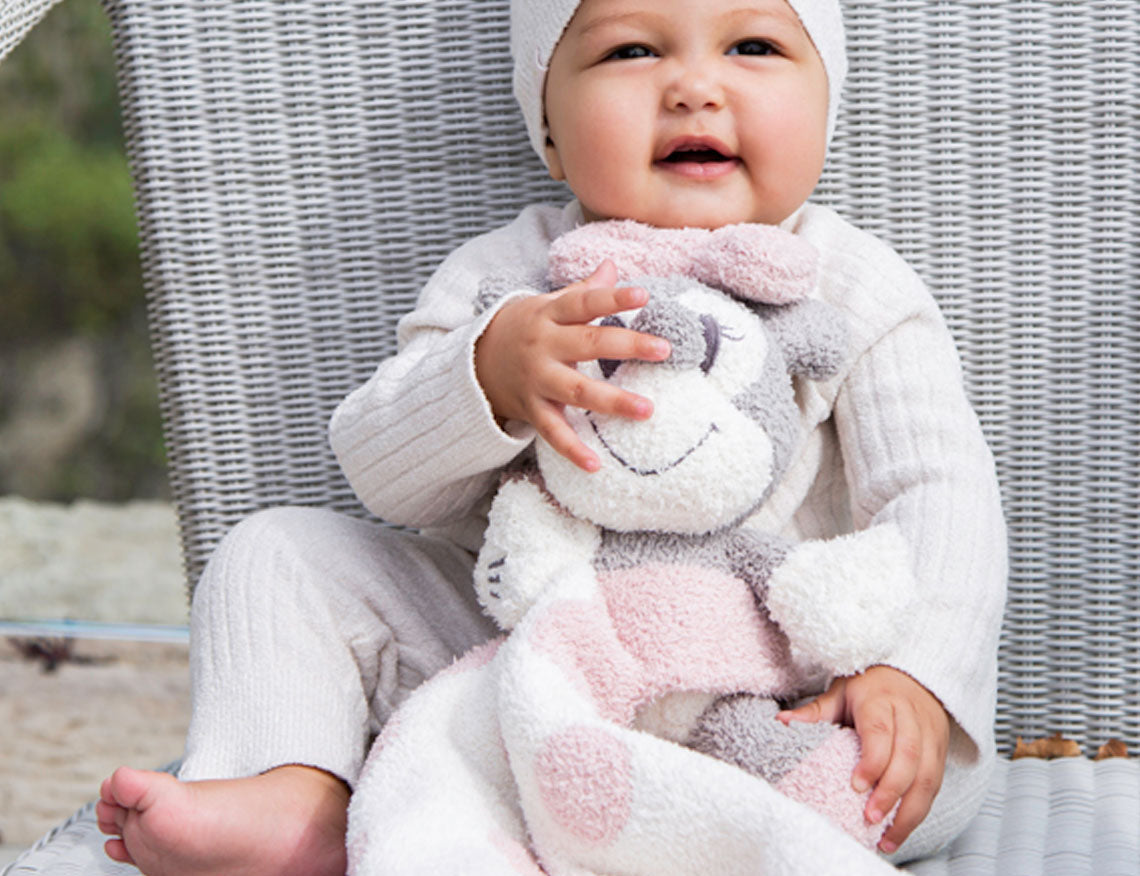 Smiling baby in a white hat holding a Barefoot Dreams Disney Blanket Buddie in Pink Bunny