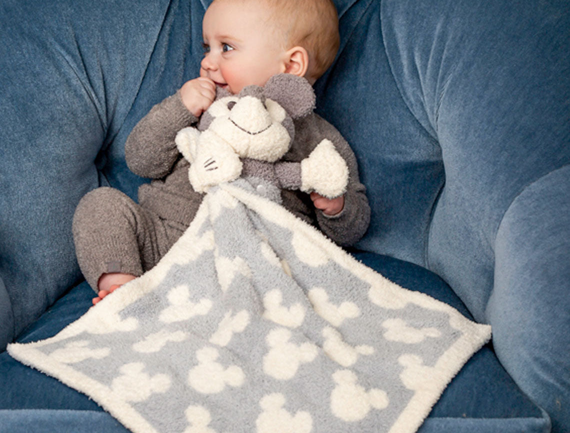 Baby in a blue chair cuddling the Barefoot Dreams Disney Blanket Buddie in Vintage Mickey Mouse