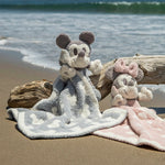 Barefoot Dreams Disney Blanket Buddies in Vintage Mickey and Vintage Minnie on a beach beside driftwood