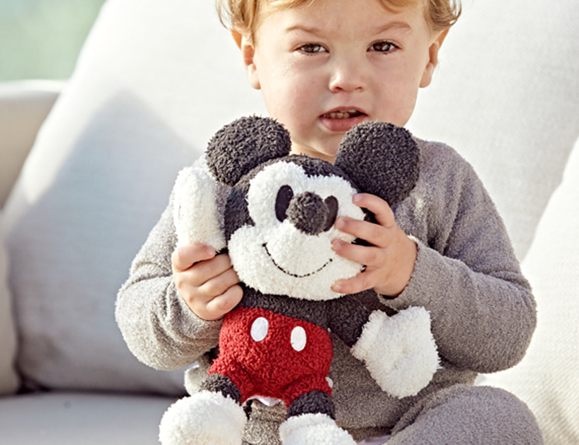 Toddler in gray pajamas hugging the Barefoot Dreams Disney Buddie in Mickey Mouse