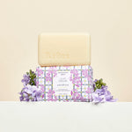 Beekman 1802 Bar Soap in Lilac Dream unwrapped on its box with fresh lilac blooms
