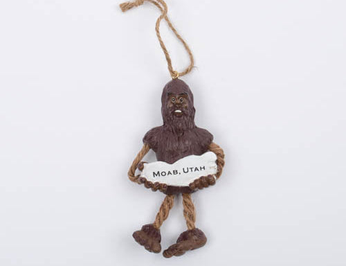 Sasquatch Ornament, brown sasquatch holding a Moab, Utah sign, with dangling rope legs and a twine hanger