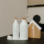 Blomus Bon Appetit Porcelain Cruet Bottles on a dark counter beside a small wooden house-shaped board