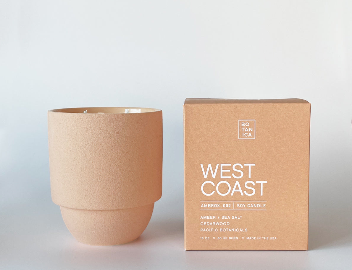 Botanica West Coast Candle in a terracotta ceramic vessel beside its orange box