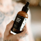 Hand holding the Broken Top Brands Birch Charcoal Man Spray amber bottle