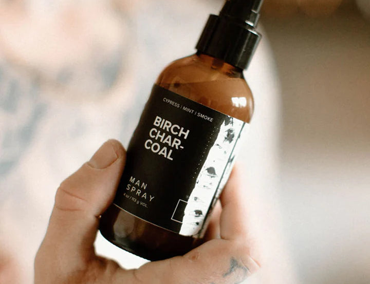 Hand holding the Broken Top Brands Birch Charcoal Man Spray amber bottle