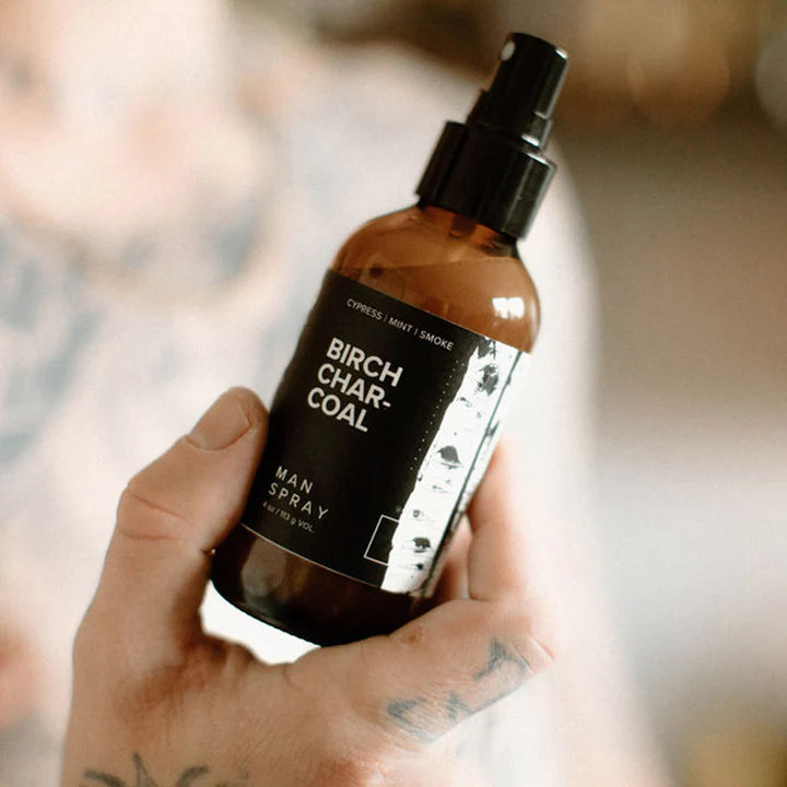 Hand holding the Broken Top Brands Birch Charcoal Man Spray amber bottle
