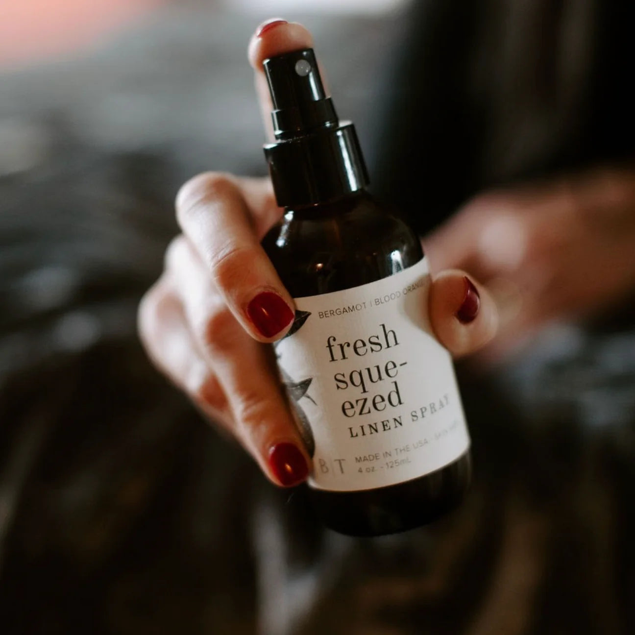 Hand with red nails holding the Broken Top Brands Fresh Squeezed Linen Spray amber bottle