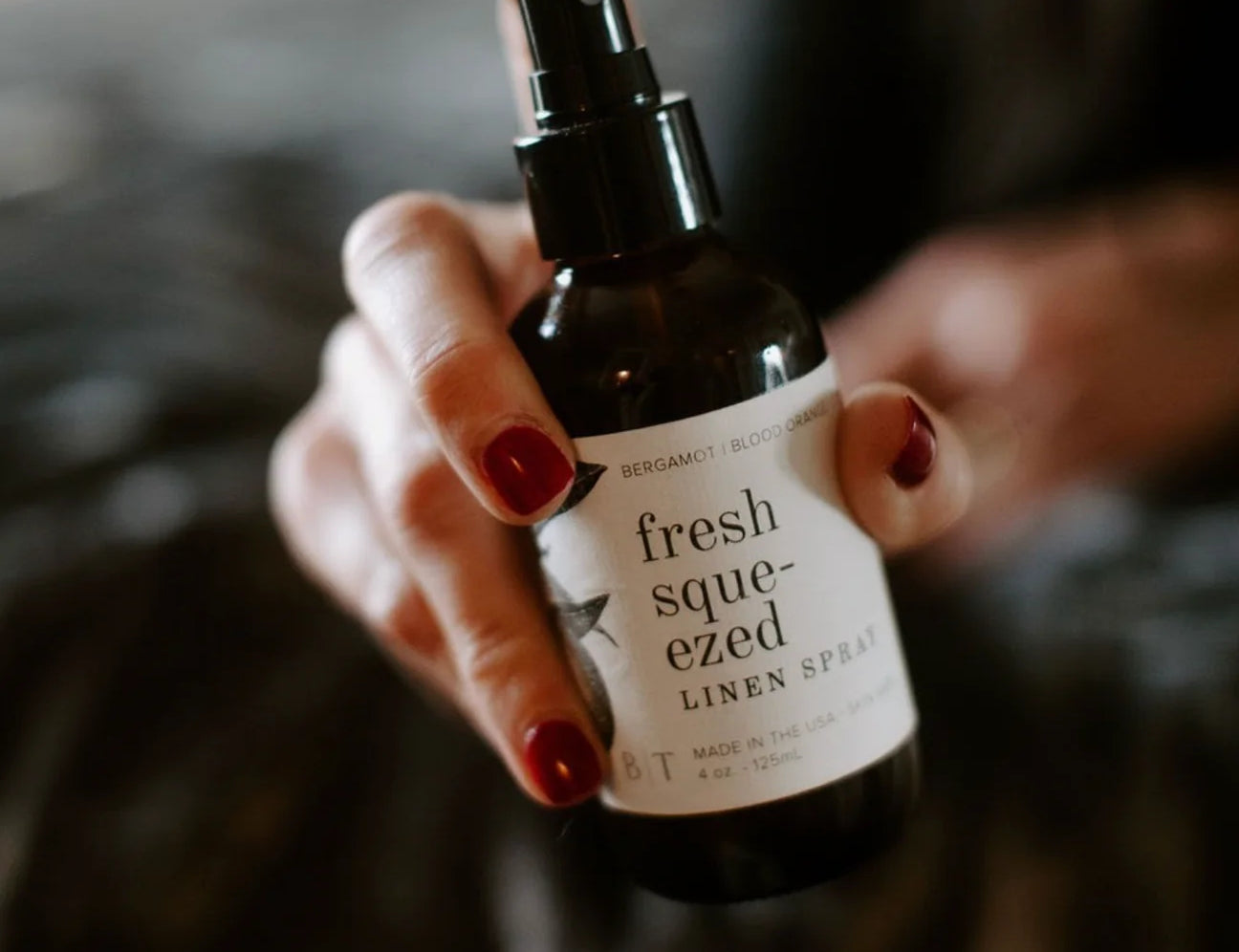 Hand with red nails holding the Broken Top Brands Fresh Squeezed Linen Spray amber bottle
