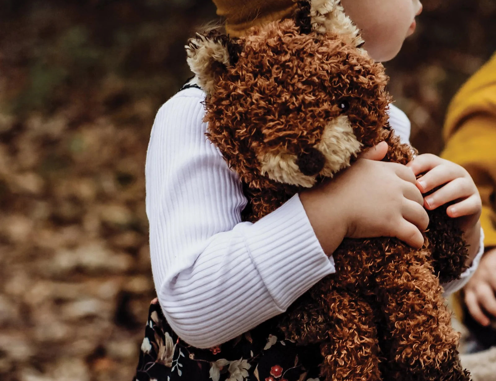 Child in a yellow hat hugging the Bunnies By The Bay Foxy The Fox Plush among autumn leaves