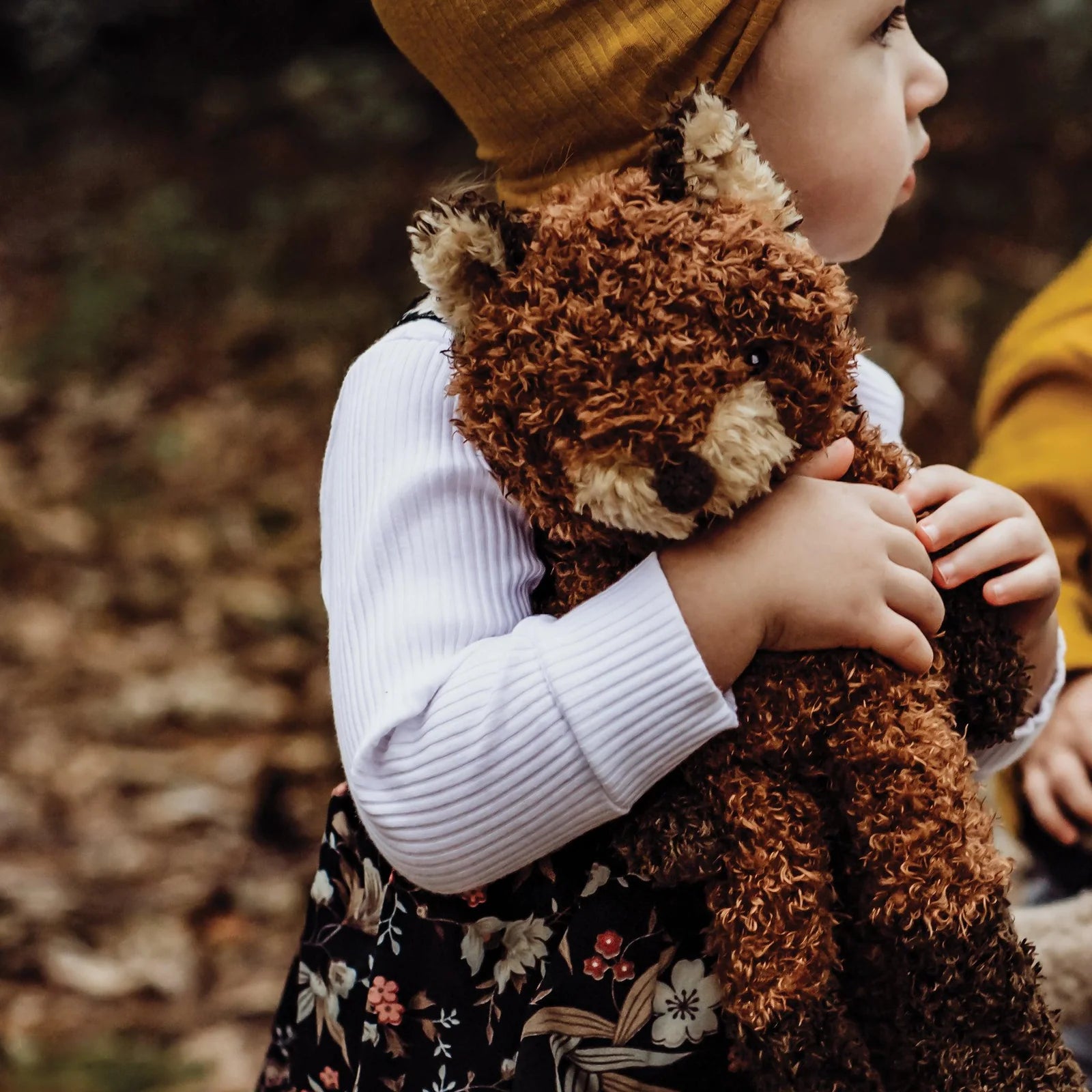 Child in a yellow hat hugging the Bunnies By The Bay Foxy The Fox Plush among autumn leaves
