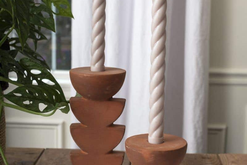 Two Cadwell Candle Holders with stacked half moon design in natural terracotta, holding twister taper candles placed on tablecloth. 