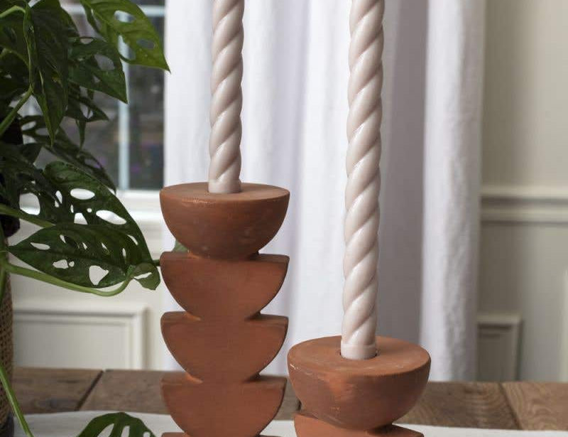 Two Cadwell Candle Holders with stacked half moon design in natural terracotta, holding twister taper candles placed on tablecloth. 