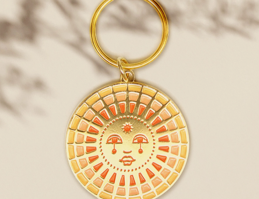 Cai & Jo Keychain, a round gold enamel sun face charm in orange and cream on a gold ring
