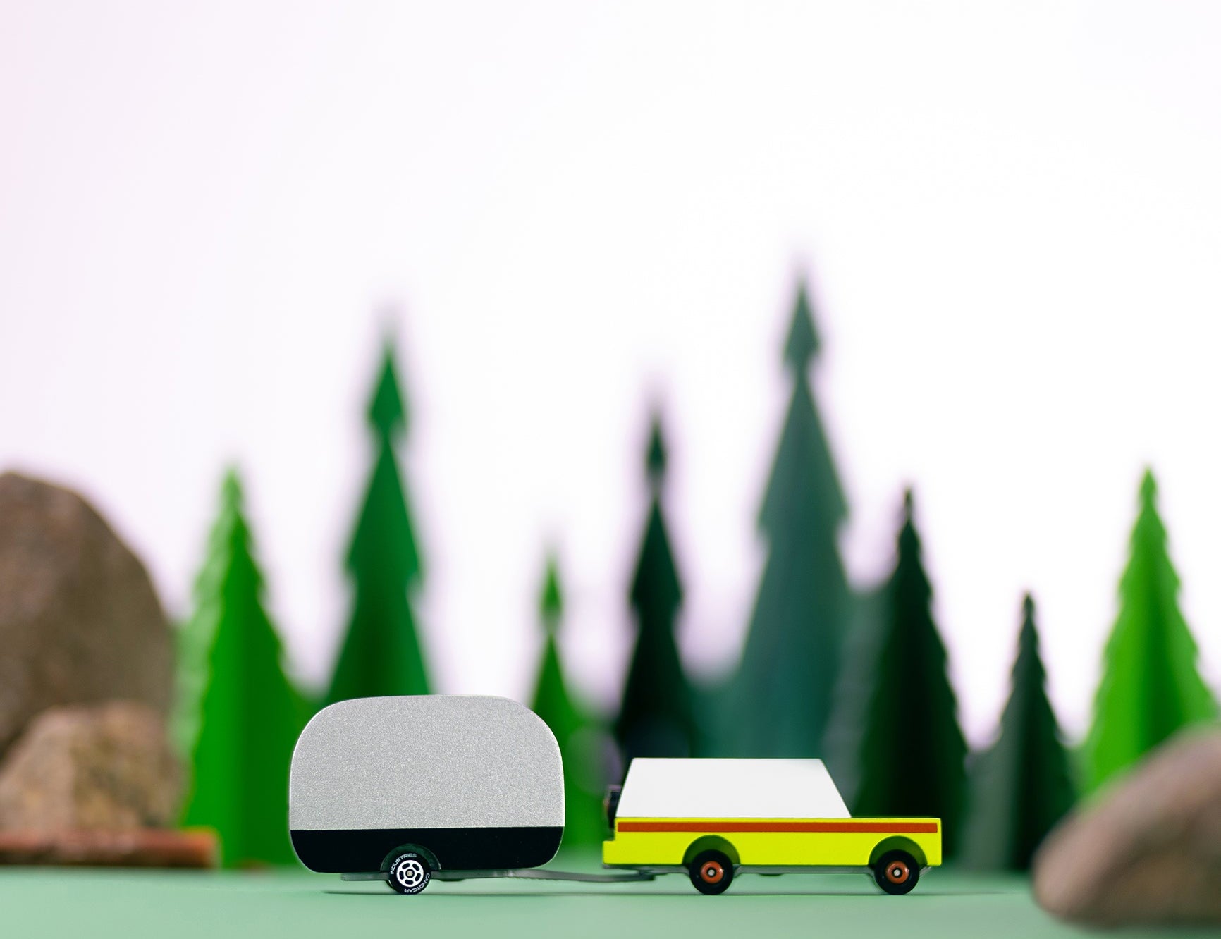 Candylab Toys Airstream Camper toy trailer towed by a yellow wooden car through a miniature pine forest scene