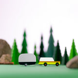 Candylab Toys Airstream Camper toy trailer towed by a yellow wooden car through a miniature pine forest scene