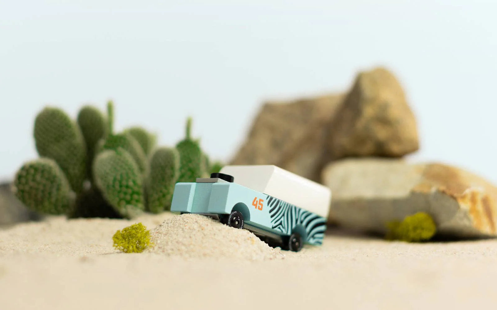 Candylab Toys Mini Zebra Drifter on sand beside a toy cactus and rocks