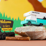 Candylab Toys Olympic Wooden RV parked on a rock beside a Welcome to Olympic National Forest sign
