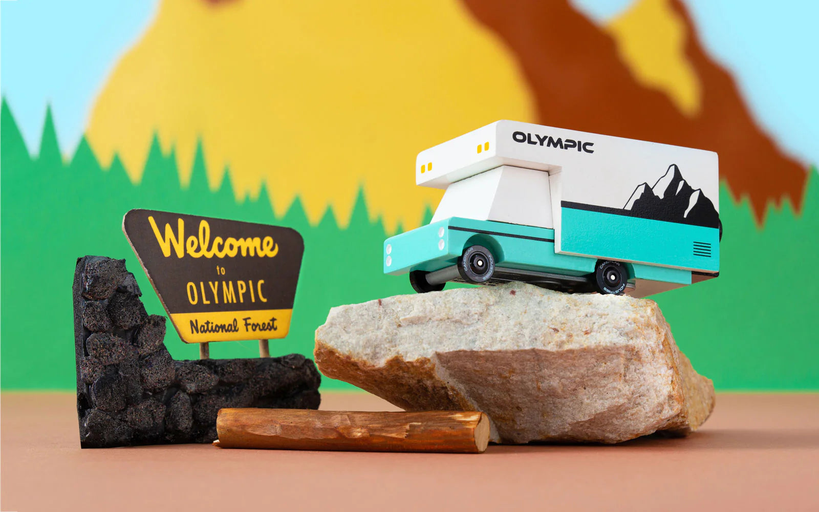 Candylab Toys Olympic Wooden RV parked on a rock beside a Welcome to Olympic National Forest sign