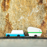 Candylab Toys Pinecone Toy Camper hitched to a blue wooden SUV on a rock ledge