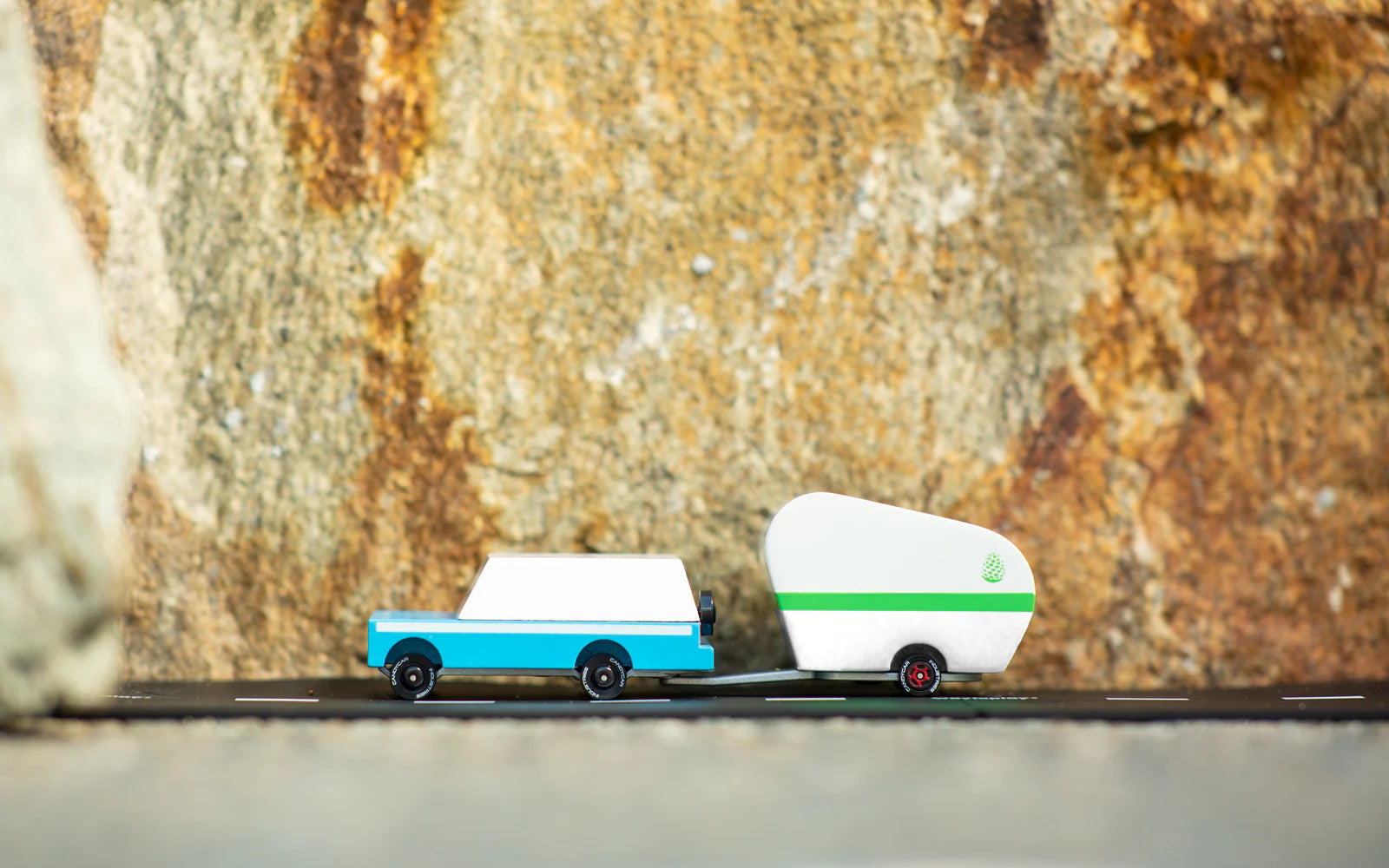 Candylab Toys Pinecone Toy Camper hitched to a blue wooden SUV on a rock ledge